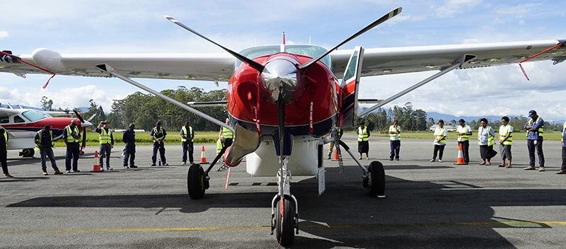 A view from the front of P2-AFD with MAF workers in hi-vis standing in a circle around the aircraft seen in the background