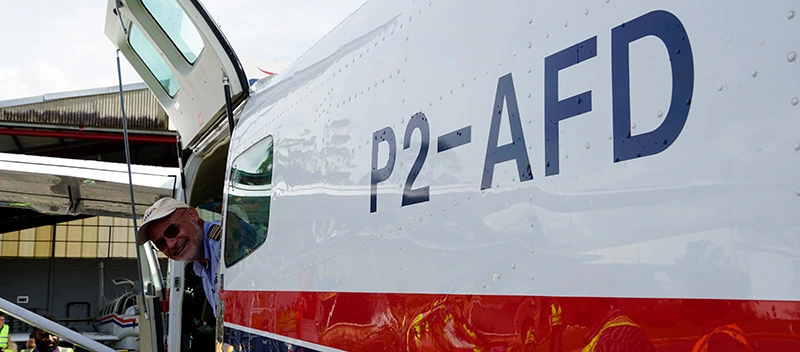 Side of aircraft showing P2-AFD written on the side and the pilot hanging his head out of the door